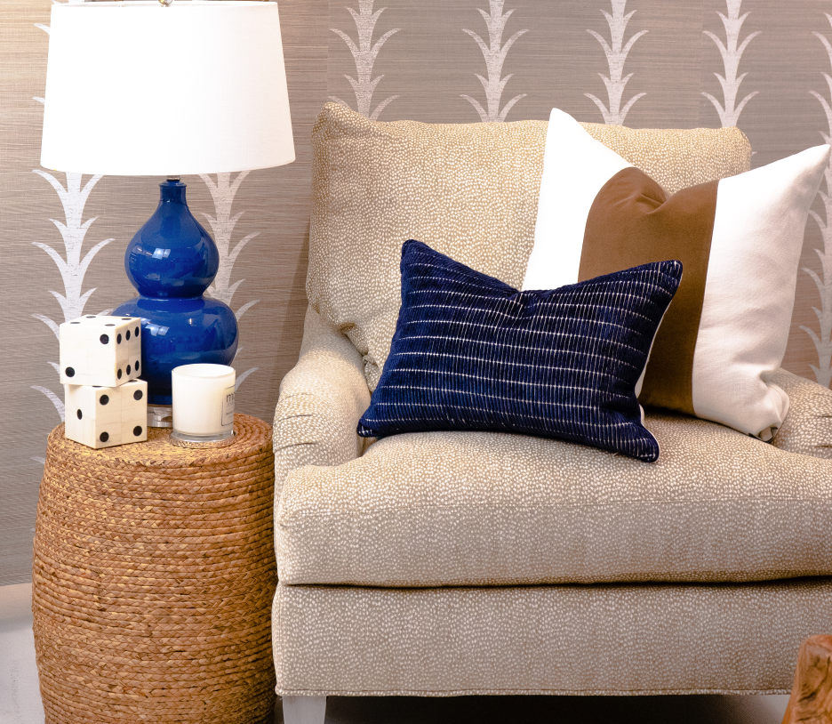 Blue lamp on wicker end table next to a cream colored chair with pillows